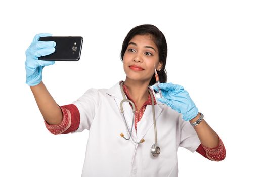 Female doctor taking selfie with stethoscope and injection by smartphone on white background.