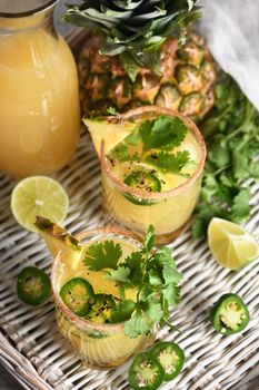 Spicy pineapple margarita with jalapeno slices, lime and cilantro sprigs