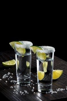 Portion of tequila, framed with a salt edge with slice lime in tall shot glasses