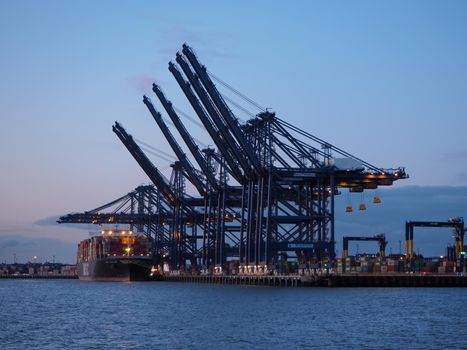 Port of Felixstowe, Suffolk, UK, March 8 2020: Cranes loading containers onto the MSC Kalina cargo ship against the dock lights at dusk