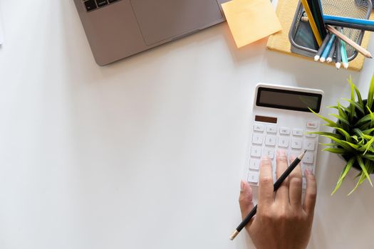 Top view hand of accountant using calculator on workplace with copy space, calculator and plant potted on white desk background, Accounting workplace concept.