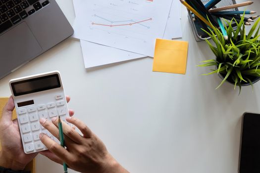 Top view hand of accountant using calculator on workplace with copy space, calculator and plant potted on white desk background, Accounting workplace concept.