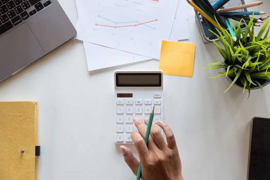 Top view hand of accountant using calculator on workplace with copy space, calculator and plant potted on white desk background, Accounting workplace concept.