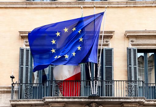 The flag of the European Community flying above the Italian flag on the balcony of a public building. Politics and economics.