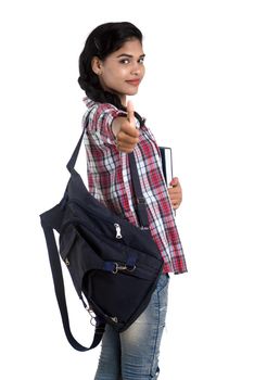 young Indian woman with backpack standing and holding notebooks, posing on a white background.