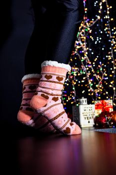 Female legs in Christmas colorful socks near Christmas tree.