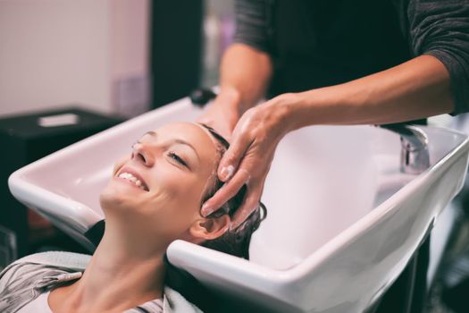 Young woman getting new hairstyle at professional hair styling saloon. Hairdresser is washing and massaging her head.