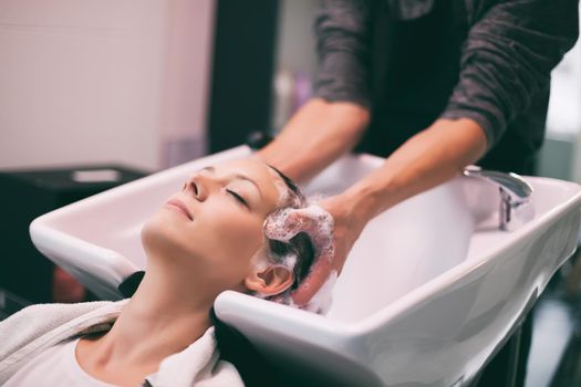 Young woman getting new hairstyle at professional hair styling saloon. Hairdresser is washing and massaging her head.