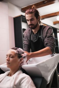 Young woman getting new hairstyle at professional hair styling saloon. Hairdresser is washing and massaging her head.