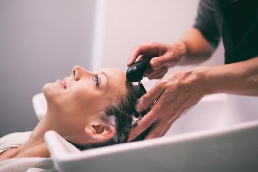 Young woman getting new hairstyle at professional hair styling saloon. Hairdresser is washing and massaging her head.