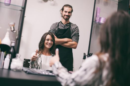 Young woman getting new hairstyle at professional hair styling saloon. She is very satisfied.