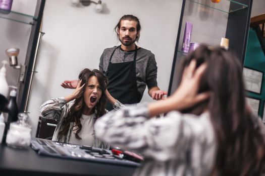 Young woman getting new hairstyle at professional hair styling saloon. She is not satisfied with her new hairstyle.