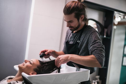 Young woman getting new hairstyle at professional hair styling saloon. Hairdresser is washing and massaging her head.