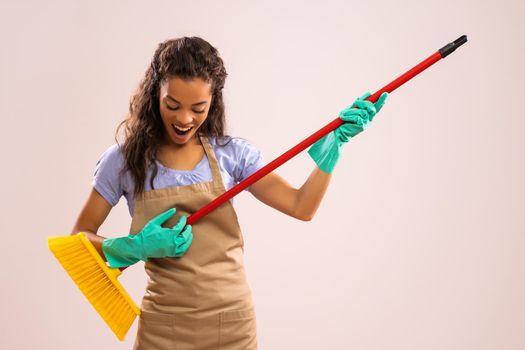 Portrait of happy and successful african-american professional maid having fun with broom.