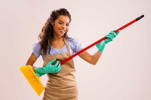 Portrait of happy and successful african-american professional maid having fun with broom.