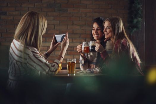 Three happy girlfriends are having fun time in pub. They are talking and drinking beer. Friendship concept.