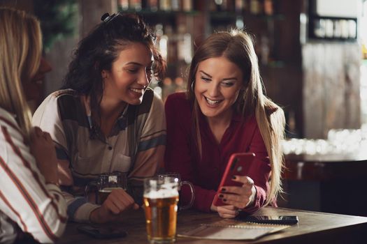 Three happy girlfriends are having fun time in pub. They are talking and drinking beer. Friendship concept.