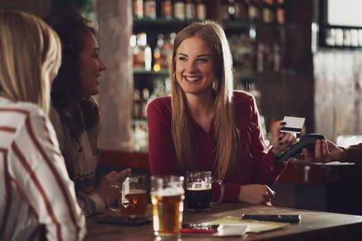 Three happy girlfriends are having fun time in pub. They are talking and drinking beer. Friendship concept.