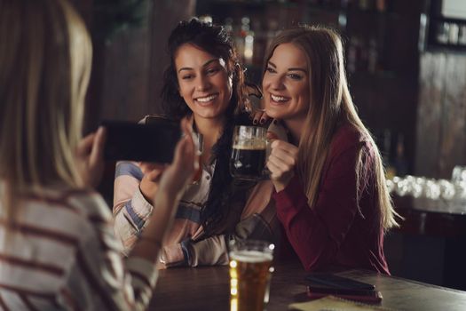 Three happy girlfriends are having fun time in pub. They are talking and drinking beer. Friendship concept.