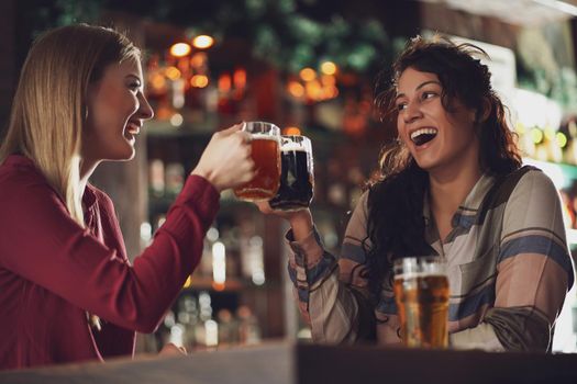 Two happy girlfriends are having fun time in pub. They are talking. Friendship concept.