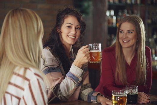 Three happy girlfriends are having fun time in pub. They are drinking beer. Friendship concept.