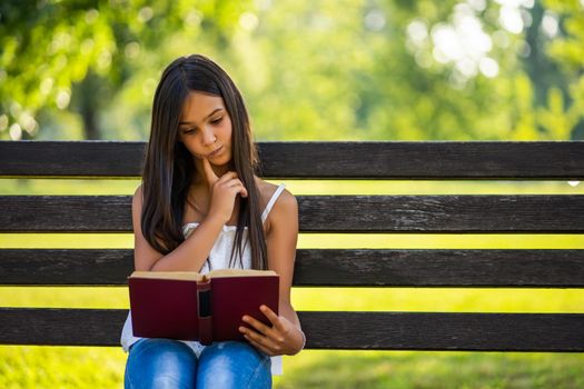 Happy little girl is reading a book in park.