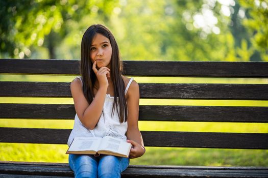 Happy little girl is reading a book in park.