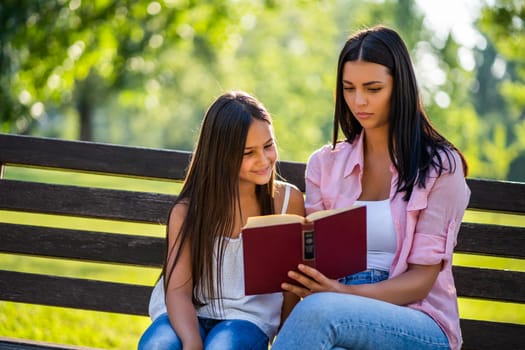 Young mother is teaching her daughter in park.