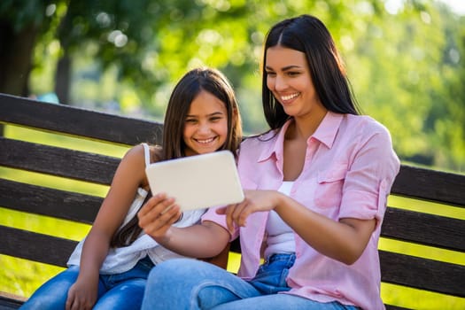 Happy family having nice time in park together. They are using digital tablet.