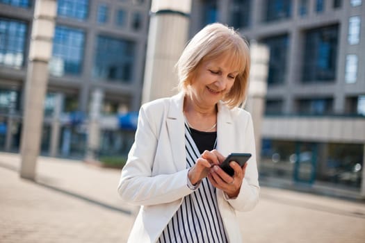 Outdoor portrait of happy senior businesswoman who is using smartphone.