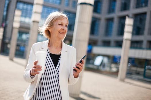 Outdoor portrait of happy senior businesswoman who is using smartphone.