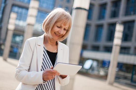 Outdoor portrait of happy senior businesswoman who is using digital tablet.