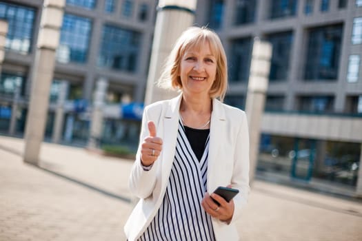 Outdoor portrait of happy senior businesswoman who is using smartphone.