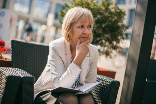 Senior businesswoman is sitting in cafe and making job plans.