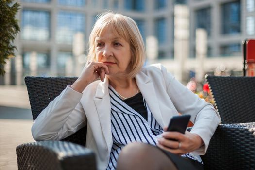 Senior businesswoman is sitting in cafe and searching for job on internet.