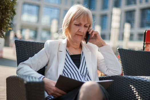 Senior businesswoman is talking on phone in cafe.