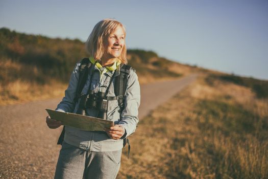 Senior woman is hiking in mountain. Active retirement. She is using map.