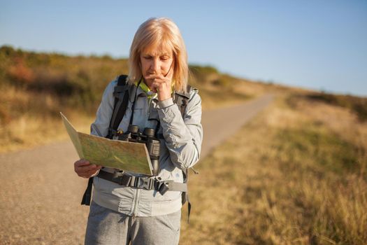 Senior woman is hiking in mountain. Active retirement. She is using map.