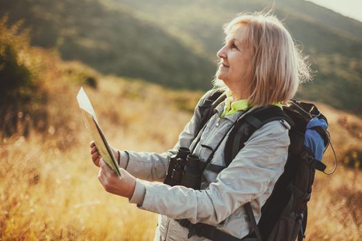Senior woman is hiking in mountain. Active retirement. She is using map.