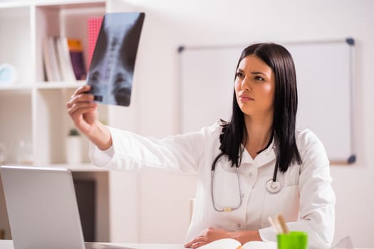 Young doctor is examining x-ray image in her office.