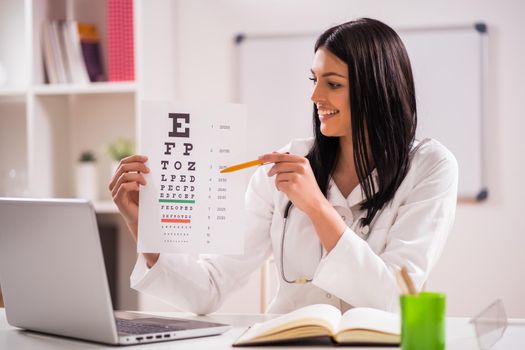 Young doctor is holding eye examination test in her office.