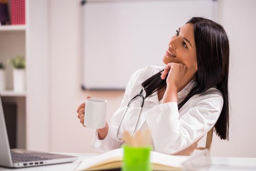 Young doctor is drinking coffee in her office.