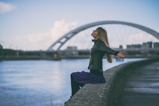 Adult woman relaxing at river bank in the city.