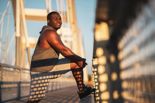 Young african-american man is exercising on the bridge in the city.