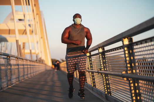 Young african-american man is jogging with protective mask on his face. Corona virus pandemic responsible behavior.
