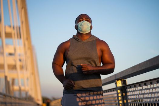 Young african-american man is jogging with protective mask on his face. Corona virus pandemic responsible behavior.