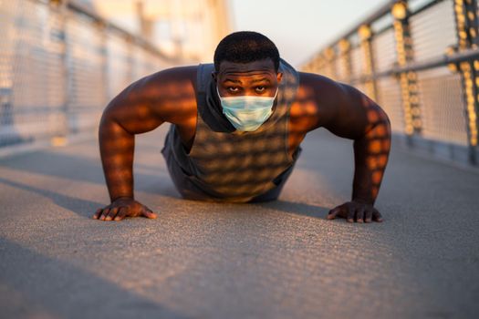 Young african-american man is exercising with protective mask on his face. Corona virus pandemic responsible behavior.