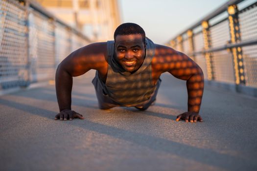 Young african-american man is exercising on the bridge in the city. He is doing push-ups.