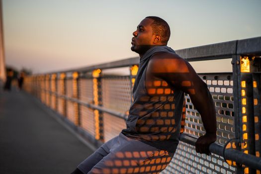 Young african-american man is exercising in sunset on the bridge in the city.