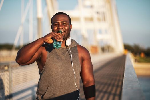 Portrait of young cheerful african-american man in sports clothing who is drinking water after exercising.